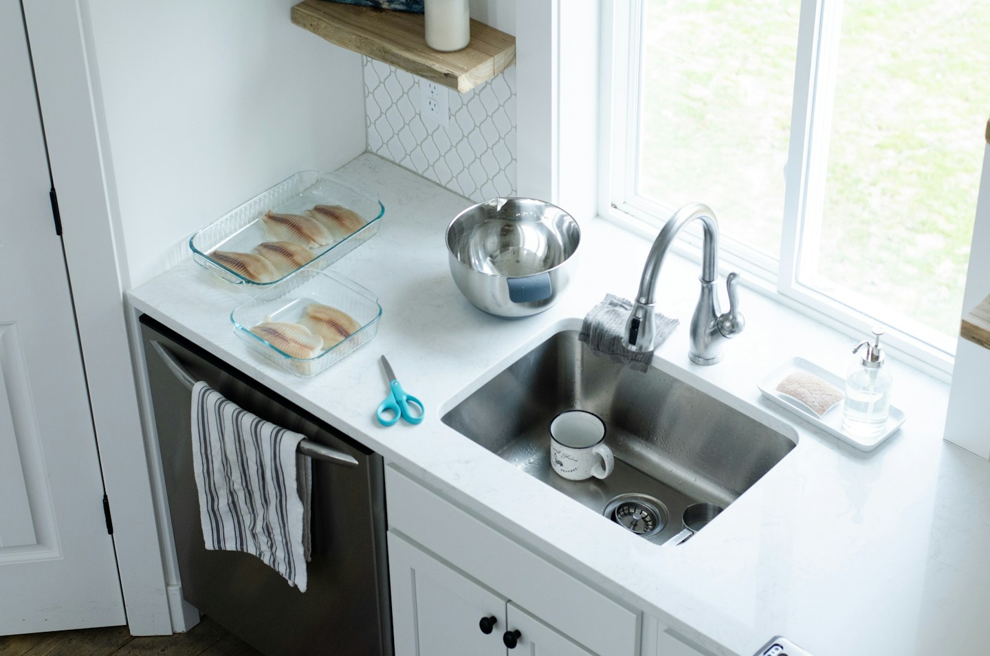 A kitchen counter with a sink, dishware, and a towel hanging below.