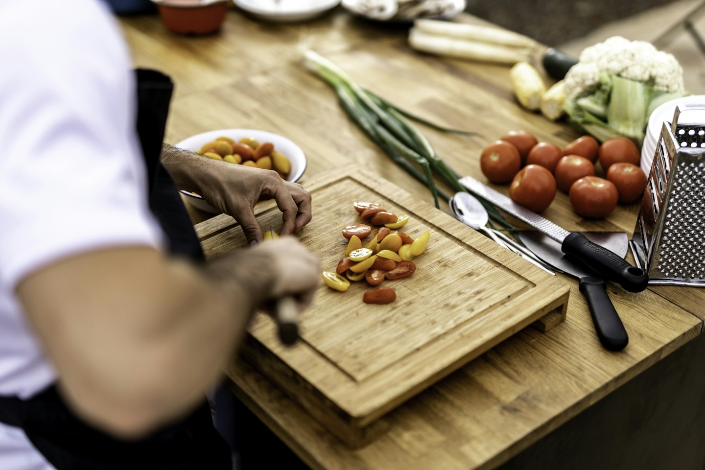 A person preparing vegetables on a wooden cutting board in a kitchen.