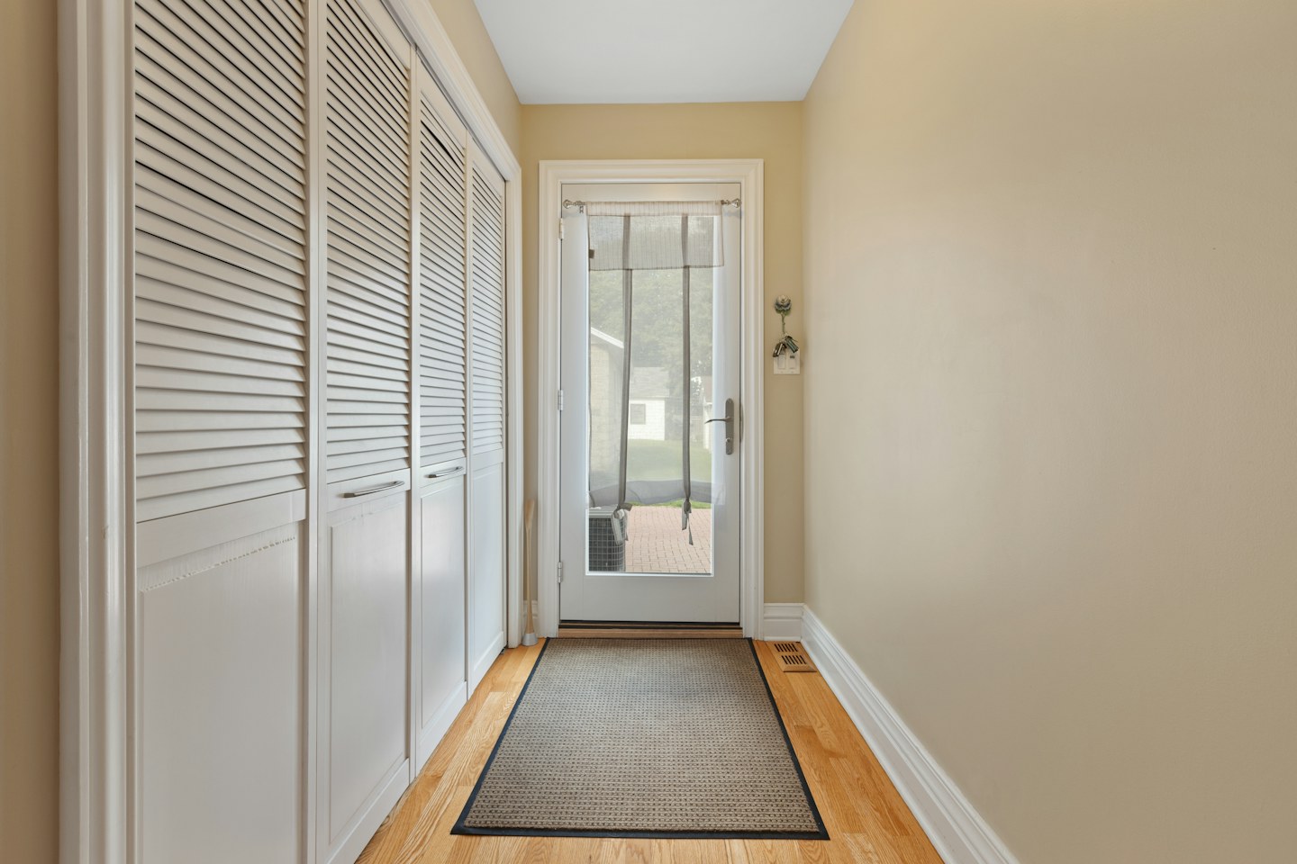 A hallway with closet doors, a glazed entrance door, and a floor mat.
