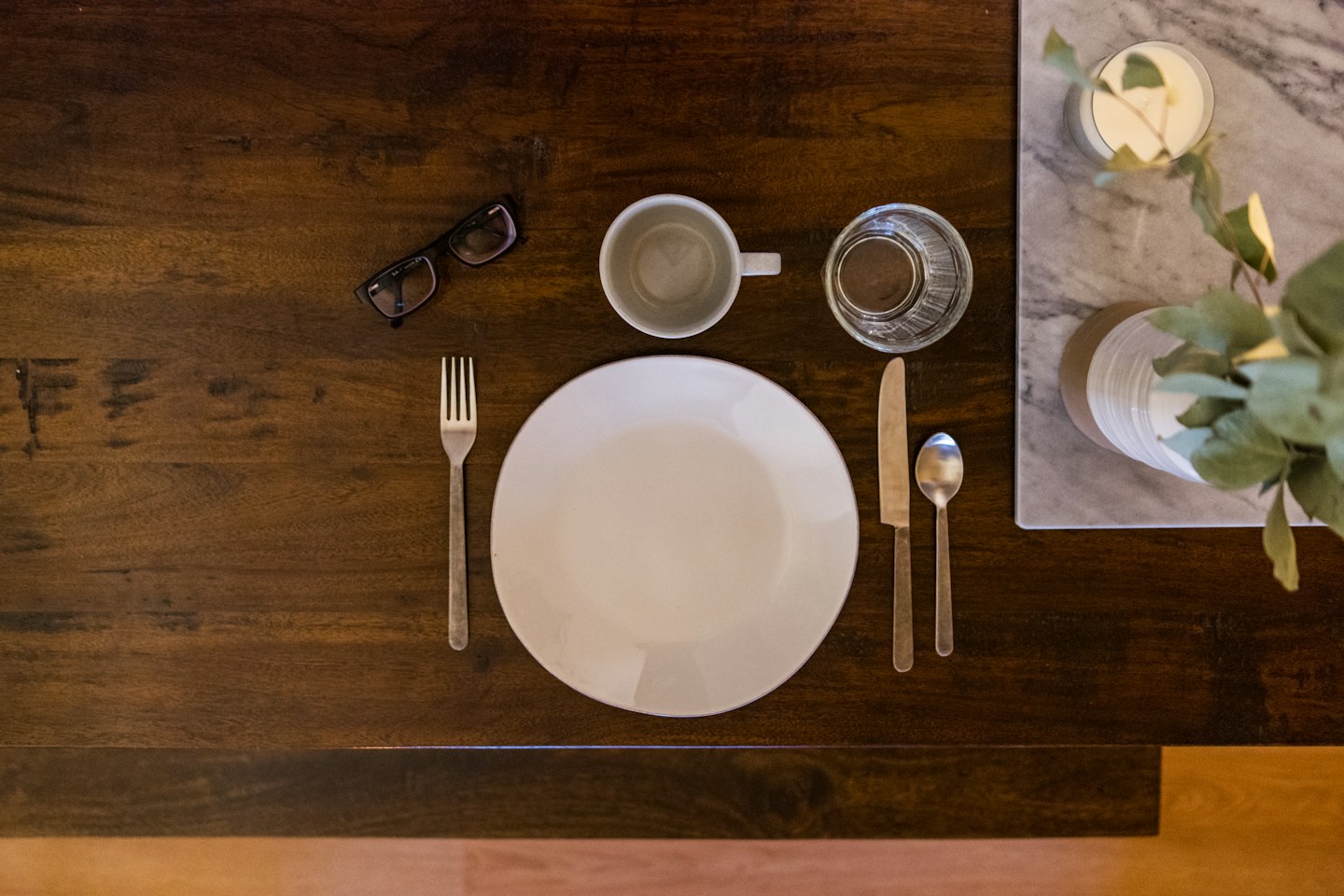 A place setting with a white plate, cutlery, cup, and glass on a wooden table.
