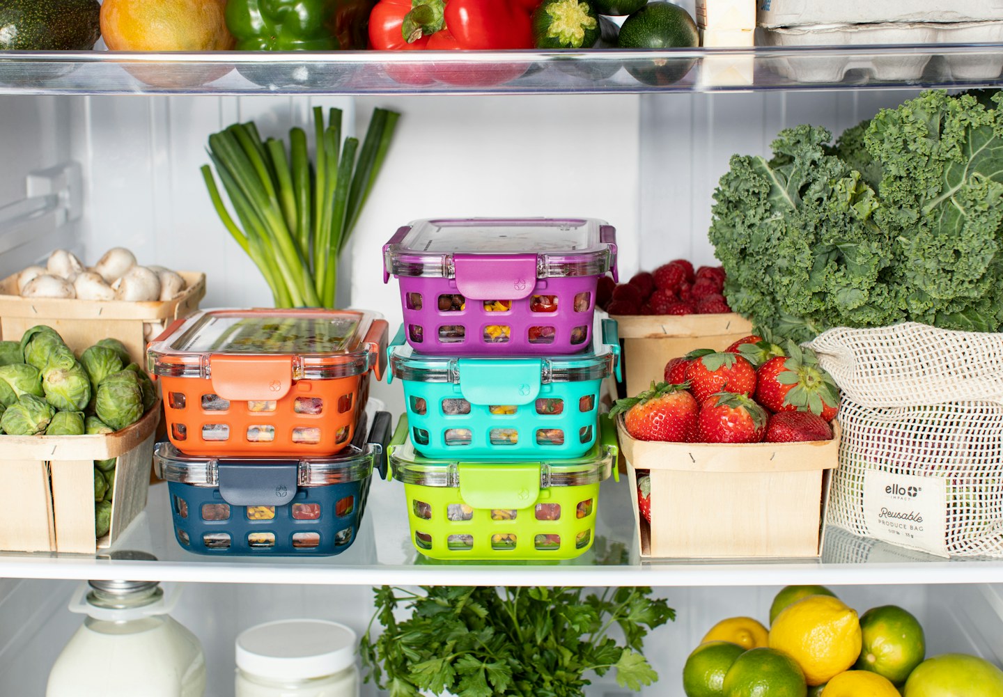An open refrigerator with colorful food containers and fresh vegetables.