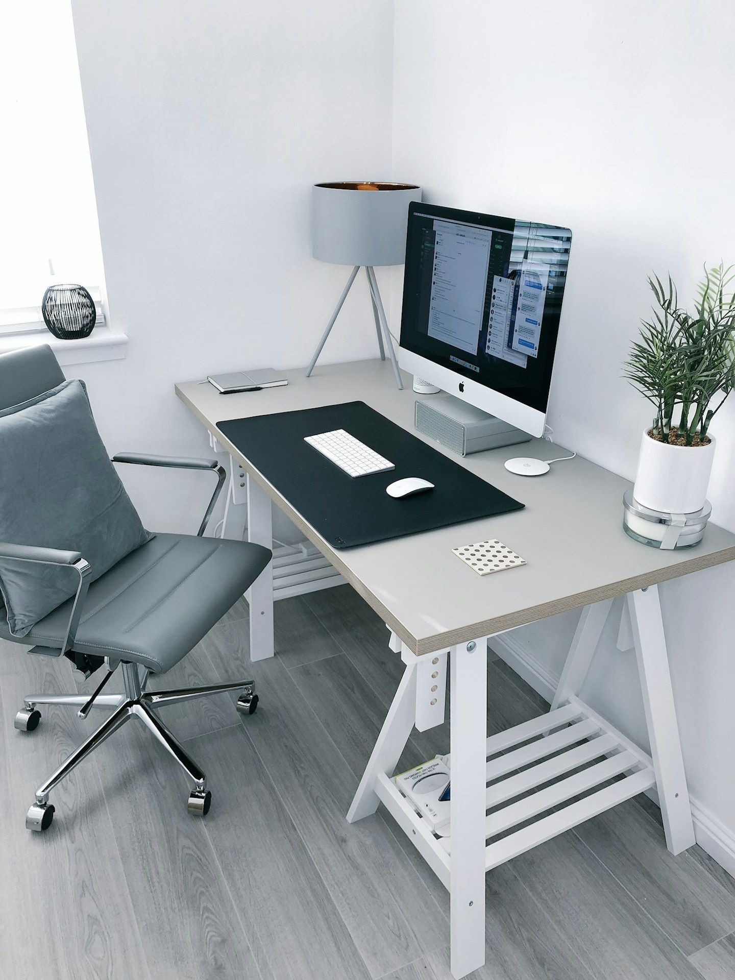 A home office with a desk, computer screens, rolling chair, and plant.