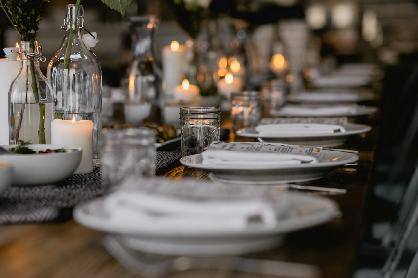 A dining table set with white plates, glasses, bottles, and candles.