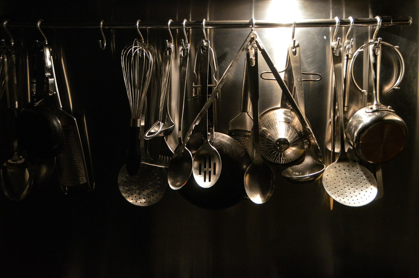 Metal cooking utensils hanging together in a kitchen.