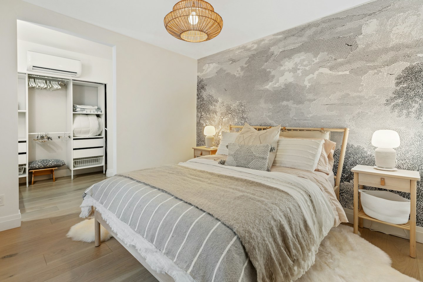 A bedroom with light bedding, a bedside table, and a textured accent wall.