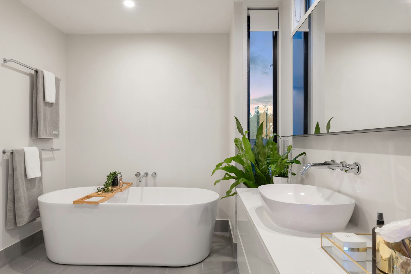A bright bathroom with a freestanding bathtub, sinks, and green plants.