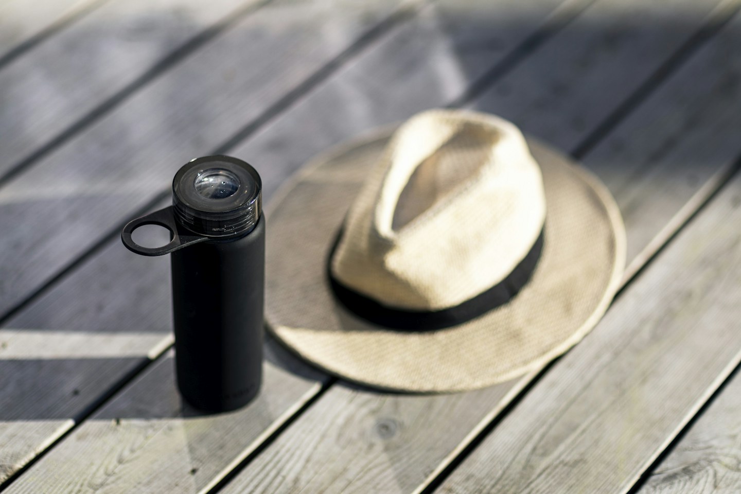 A reusable drinking bottle and a straw hat on a wooden outdoor table.