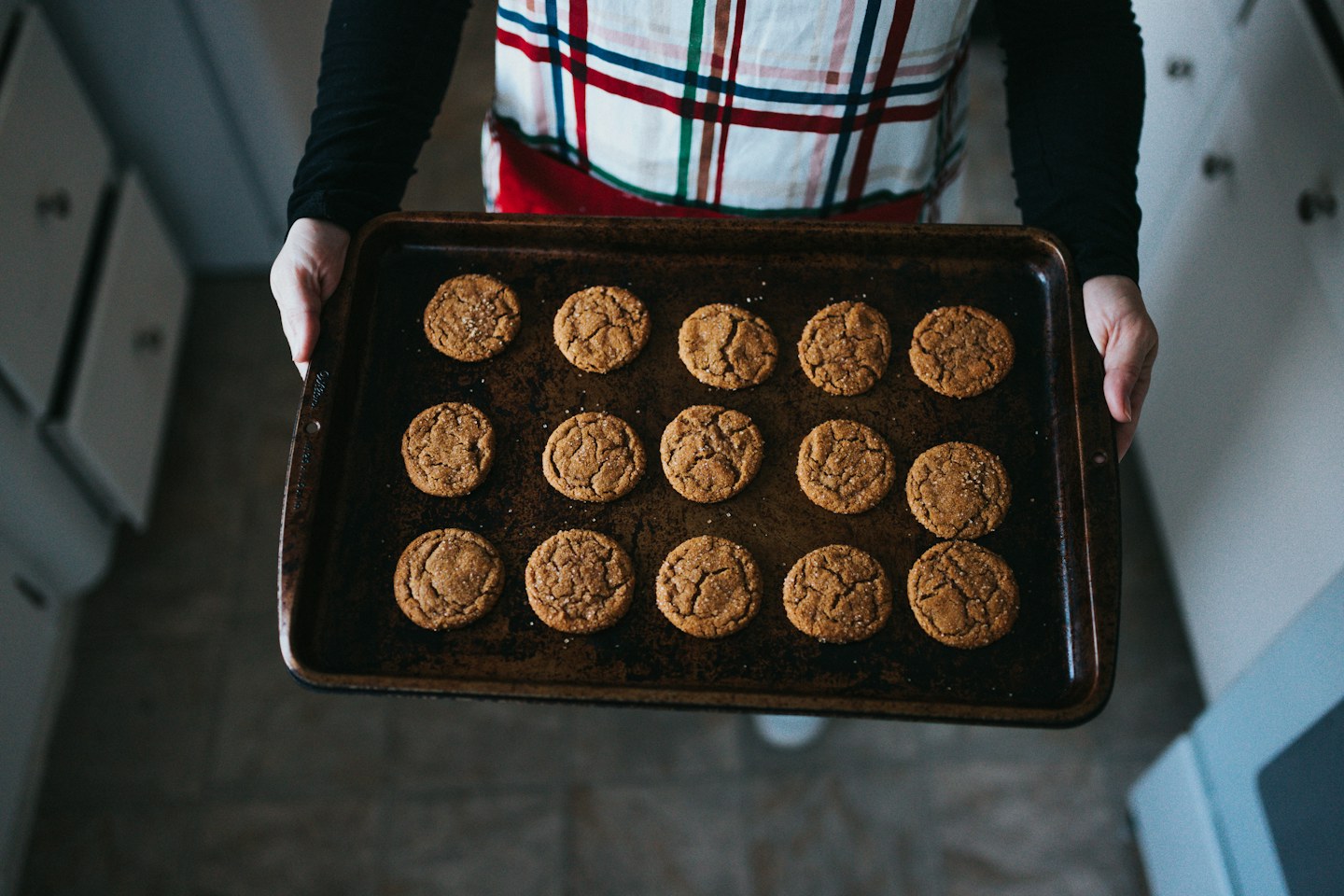 A person holding a baking tray filled with freshly baked cookies.