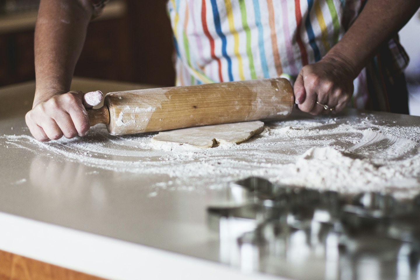 A person rolling dough on a flour-dusted kitchen surface.