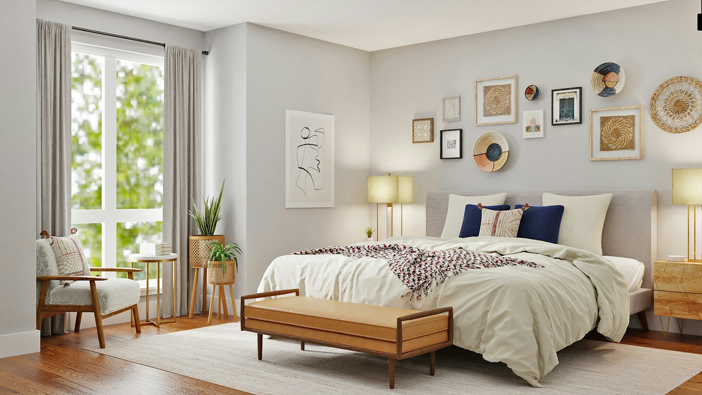 A sunlit bedroom with a made bed, leather bench, and framed wall art.