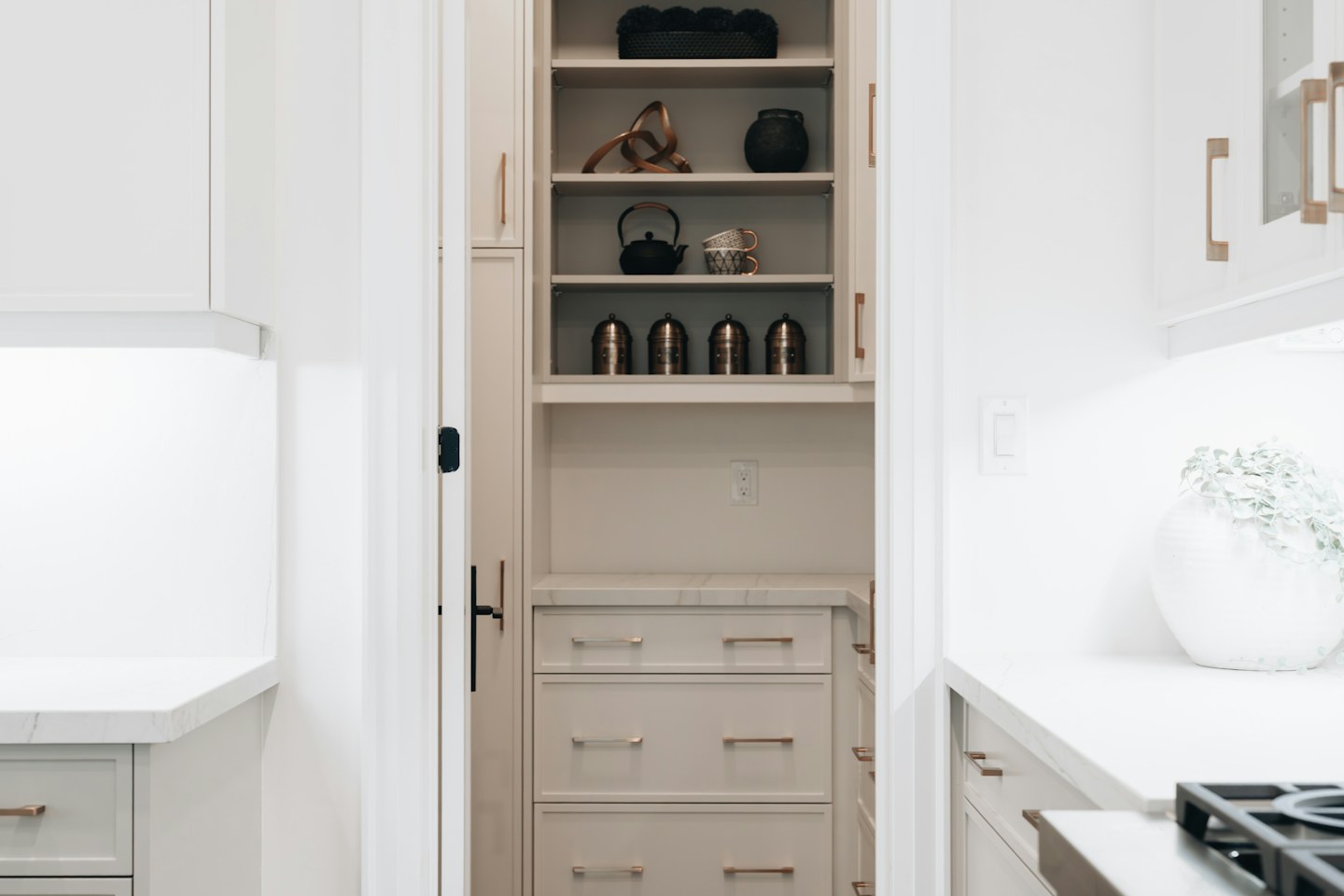 A compact pantry with open shelves, jars, and storage drawers.